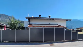 Rückansicht eines Hauses mit moderner Zaunanlage und Bergblick unter klarem blauen Himmel.