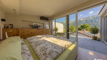 Helles Schlafzimmer mit Holzboden, großen Glasfronten und Zugang zu einer Terrasse mit Bergblick.
