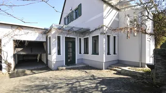 Vorderansicht des Hauses mit integrierter Garage und gepflasterter Einfahrt unter klarem Himmel.