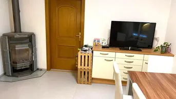 Gemütlicher Wohn-Essbereich mit Kaminofen, Holztür und einem Sideboard mit Fernseher.