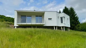 Modernes weißes Haus auf einem grünen Hügel mit Balkon und weitem Blick.