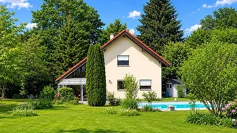Großzügiger Gartenbereich mit Einfamilienhaus, Swimmingpool und altem Baumbestand unter blauem Himmel.