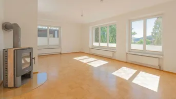 Helles Wohnzimmer mit Parkettboden, Kaminofen und großen Fenstern mit Blick ins Grüne.