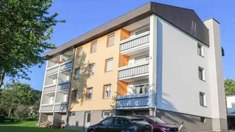 Mehrfamilienhaus mit farbiger Fassade, mehreren Balkonen und umliegender Grünfläche unter blauem Himmel.
