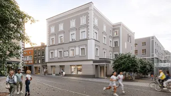 Graues Gebäude mit klassischer Fassade an einer belebten Straße mit Geschäften und Passanten.
