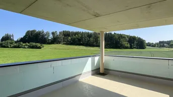 Geräumige Loggia mit weitem Blick über grüne Felder und Wälder unter blauem Himmel.