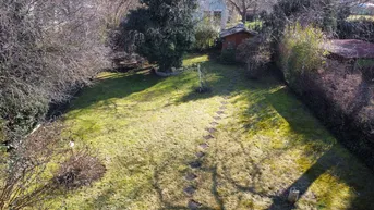 Luftaufnahme des weitläufigen Gartens mit Rasenfläche, Bäumen und einem Gartenhaus.