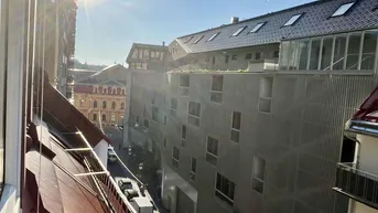 Sonnige Aussicht auf eine städtische Straße mit Gebäuden und parkenden Autos.