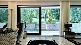 Helles Wohnzimmer mit großen Glasschiebetüren, die zum gepflegten Garten und einer Terrasse führen.