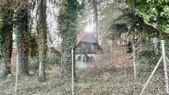 Rustikales Haus, umgeben von Bäumen und einem Zaun, in einer bewaldeten Umgebung.