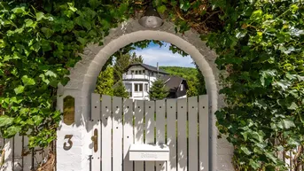Eingangstor mit üppigem Efeu bewachsen, das den Blick auf die dahinterliegende Villa freigibt.