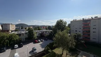 Blick über einen Parkplatz und Wohngebäude in einer städtischen Umgebung unter blauem Himmel.