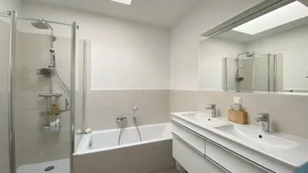 Modernes Badezimmer mit Badewanne, Duschkabine, Doppelwaschbecken und Oberlicht für viel Tageslicht.