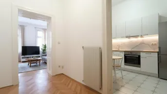 Heller Flur mit Fischgrätparkett, der zu einem visualisierten Wohnzimmer und einer Küche führt.