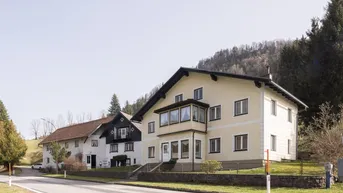 Ländliche Häusergruppe mit traditioneller Architektur und Bergblick an einer Straße gelegen.
