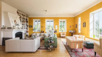 Helles Wohnzimmer mit gelben Wänden, Kamin und Holzboden, reich an Büchern und Kunst.