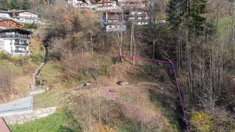Luftaufnahme eines Baugrundstücks in Hanglage mit ländlicher Umgebung und angrenzenden Häusern.