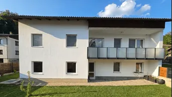 Modernes Haus mit weißer Fassade, Balkon mit Glasgeländer und gepflegtem Rasen.