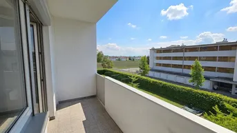 Heller Balkon mit Blick ins Grüne und auf die umliegende Bebauung unter blauem Himmel.