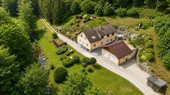 Luftaufnahme eines Landhauses mit Doppelgarage, umgeben von üppigem Grün und Wald.