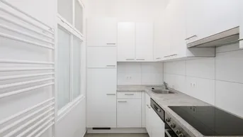 Moderne, schmale Küche mit weißen Schränken, Induktionskochfeld und Fenster.