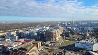 Weitläufige Luftaufnahme einer städtischen Landschaft mit markanten Gebäuden und Industrieanlagen bei Tag.
