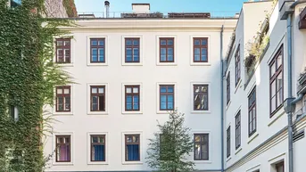 Ruhiger Innenhof mit weißer Fassade, vielen Fenstern und begrünten Wänden.