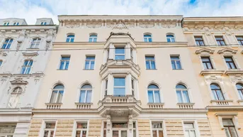 Historische Fassade eines Altbaus mit eleganten Verzierungen und Erkerfenstern unter blauem Himmel.