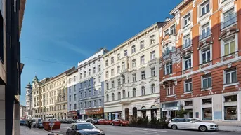Blick auf eine belebte Stadtstraße mit historischen Gebäuden und parkenden Autos.