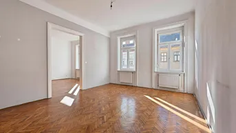 Helles Zimmer mit Fischgrätparkettboden und zwei großen Fenstern, das viel Tageslicht hereinlässt.