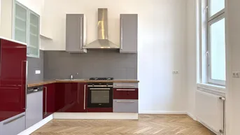 Moderne Einbauküche mit roten und grauen Fronten, ausgestattet mit Backofen und Dunstabzug.