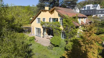 Ein charmantes gelbes Haus mit rotem Ziegeldach, umgeben von üppigem Grün und Bäumen, in einer hügeligen Landschaft.