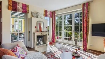 Helles Wohnzimmer mit Kamin, großen Fenstern und Zugang zur Terrasse, geschmückt mit farbenfrohen Vorhängen.