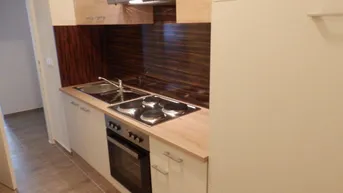 Moderne Küchenzeile mit Kochfeld, Backofen und Holzoptik-Arbeitsplatte in hellem Design.
