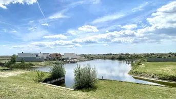 Weitläufige Seenlandschaft mit modernen Häusern am Ufer unter blauem Himmel.
