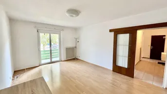 Helles Wohnzimmer mit Parkettboden, weißen Wänden und Zugang zu einem Außenbereich.