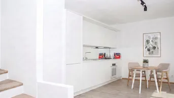 Moderne, helle Küche mit weißen Schränken, integrierten Geräten und einem kleinen Essbereich.