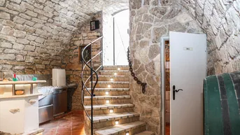 Gewölbekeller mit Natursteinwänden, beleuchteter Treppe, kleiner Bar und Zugang zur Gästetoilette.