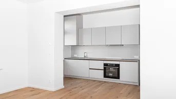 Moderne Einbauküche in hellem Grau mit integriertem Backofen und Induktionskochfeld, offen gestaltet mit Holzfußboden.