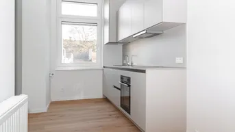 Moderne Einbauküche mit hellen Schränken, integriertem Backofen und Fenster.