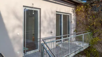 Nahaufnahme der Fassade mit Balkonzugang und Metallgeländer, umgeben von Kletterpflanzen an der Wand.