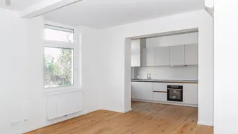 Heller Wohnbereich mit Holzfußboden und Zugang zur modernen Einbauküche.