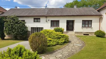 Traditionelles Einfamilienhaus mit gepflegtem Vorgarten, Steinweg und grünen Büschen unter blauem Himmel.