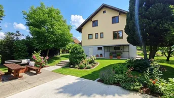 Gepflegter Gartenbereich mit Sitzgelegenheiten und Blick auf das Wohnhaus unter blauem Himmel.