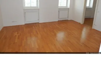 Helles, leeres Wohnzimmer mit schönem Parkettboden und zwei Fenstern, die viel Tageslicht hereinlassen.