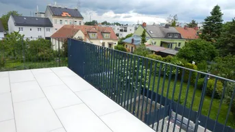 Große geflieste Terrasse mit dunklem Geländer und Blick auf die umliegende Wohngegend und Gärten.