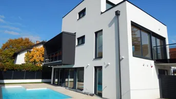 Moderne weiße Villa mit klaren Linien, großem Pool und gepflegtem Gartenbereich.