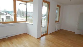 Helles, leeres Zimmer mit Parkettboden und großen Fenstern, die viel Tageslicht hereinlassen.