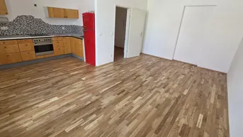 Heller offener Wohnbereich mit integrierter Küche, Holzfußboden und einem auffälligen roten Kühlschrank.