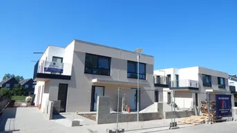 Moderne Doppelhaushälfte im Bau mit klaren Linien und Balkonen unter blauem Himmel.